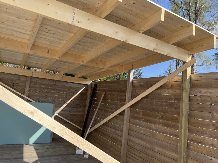 Bygget av ett träskjul med tak och inramade väggar, del av ett projekt för sommarens fotbollskvällar, med trästöd och dagsljus.