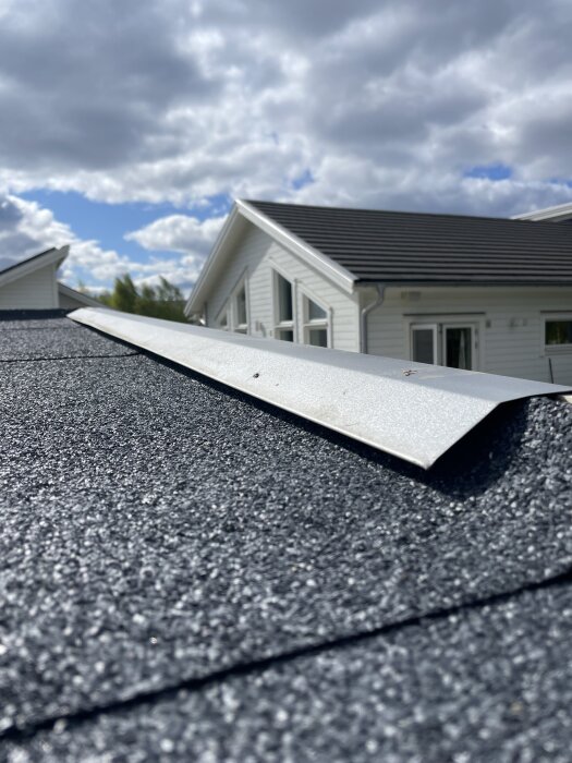 Nylagt tak med svart takpapp och silverfärgad avrinning, blå himmel och hus i bakgrunden.