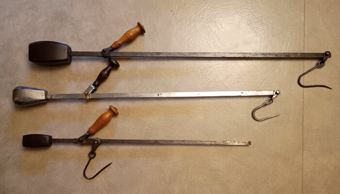 Tre besmanvågar med trähandtag och metallkrokar ligger på ett bord, användes för att väga strömming på fyrtiotalet i Vasa.