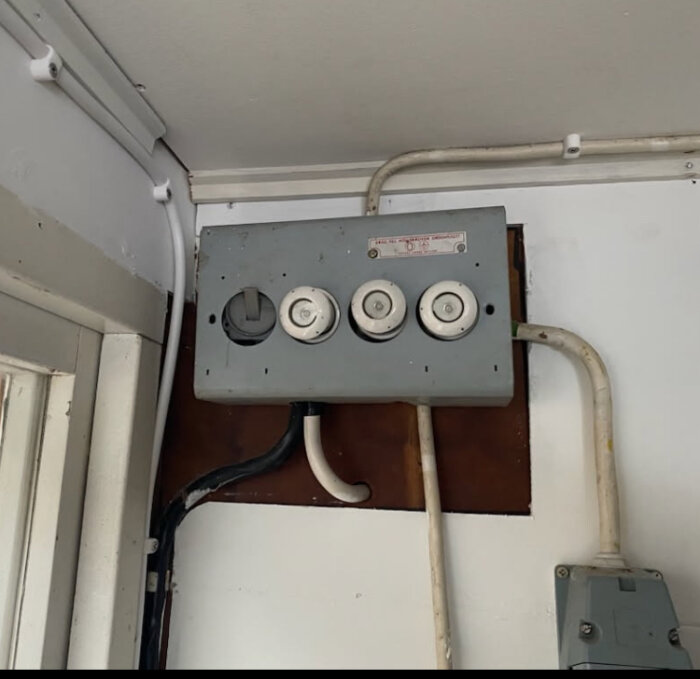 Electrical panel with three fuses and various cables, mounted on a white wall inside an indoor space.