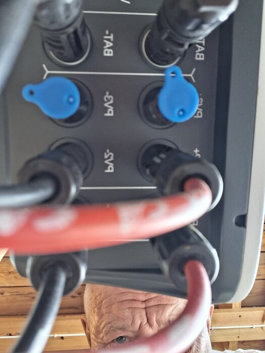 Bild på växelriktarens anslutningspanel med runda kontakter, uppmärksammat av en person som tittar in i kameran.