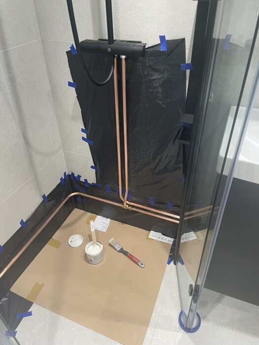 Kopparrör i badrum med skyddspapper och färgbrickor, förberett för målning med elementfärg och mattsvart lackfärg.