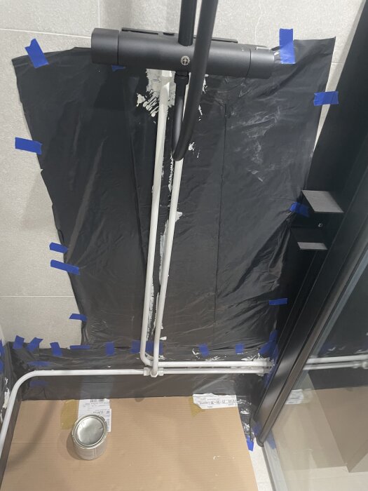 Rörmålning pågår med mattsvart färg i badrum, skyddspapp och tejp syns runt om. En burk med färg står på golvet.