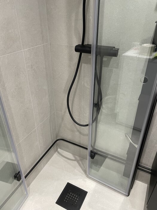 Svartmålade rör och duschdetaljer i ett färdigrenoverat badrum med glasdusch och ljust kakel.