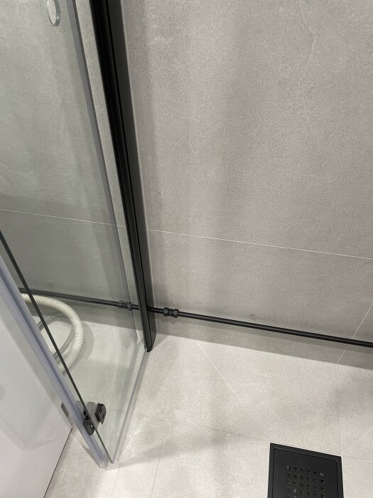 Målat badrumsrör i mattsvart färg med glasdörr på dusch och ljust kakelgolv.