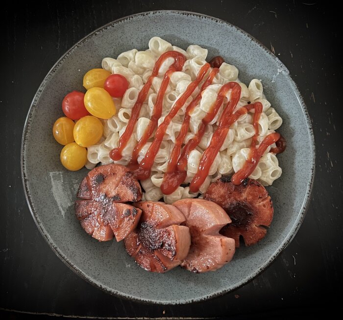 Tallrik med stuvade makaroner, stekt falukorv, nyskördade tomater och ketchup.