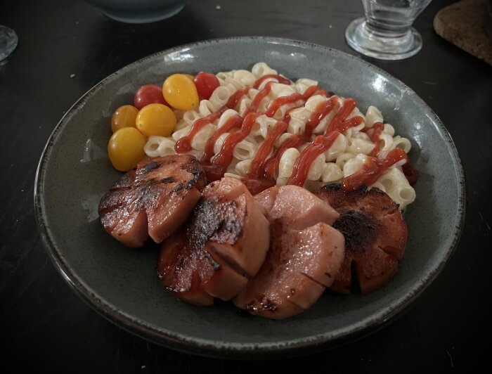 Stuvade makaroner med ketchup, stekt falukorv och nyskördade tomater på en tallrik.