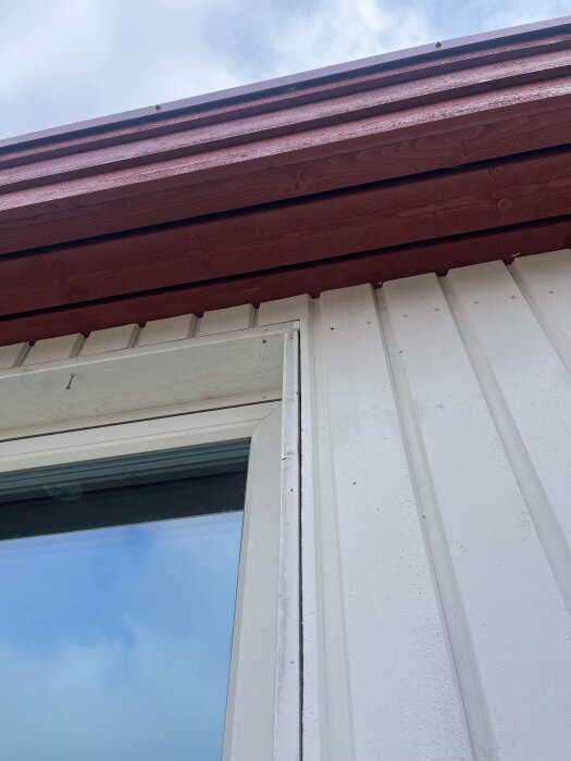 Fönster med avtagit fönsterfoder på en vit fasad under ett rött takfäste; diskussion om montering av nya fönsterbleck.