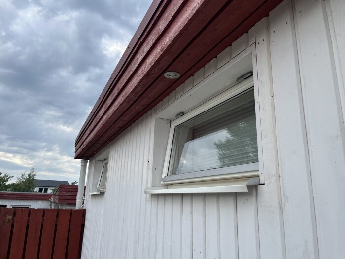 Fasad av ett hus med vita träpaneler och röda detaljer, visar fönster med monterade fönsterbleck, utan fönsterfoder.