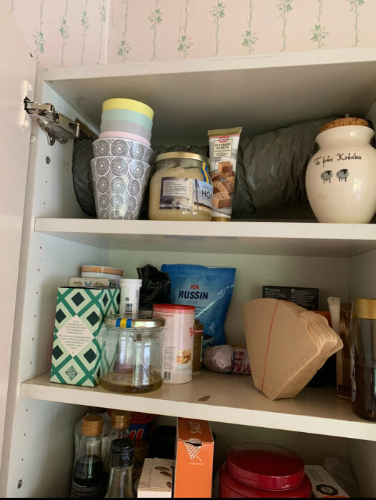 Skåp med varierande köksvaror och förpackningar, inklusive tepåsar, röd burk, och en blå påse.