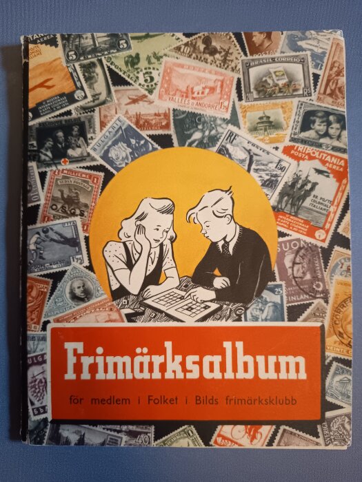 Framsidan av ett frimärksalbum med illustration av två barn vid ett bord, omgiven av olika internationella frimärken.