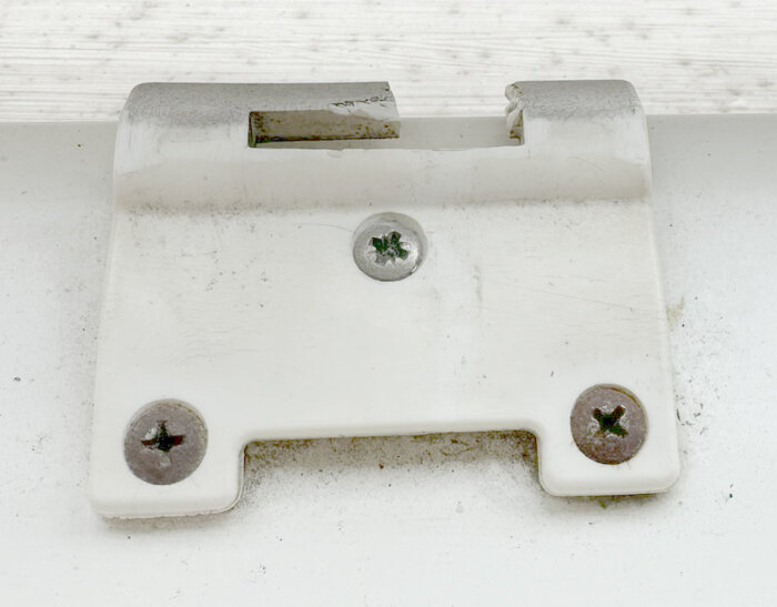 Plastbeslag till fönster med två skruvar, sprucket och gammalt.