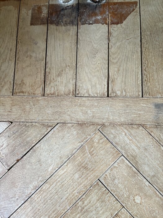 Gammal fiskbensparkett i ek med slitage och märken, vitlaserat utseende och synliga springor, redo för renovering och behandling med hårdvaxolja.