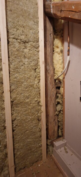 Väggkonstruktion med isolering, träreglar och en synlig trästolpe utan isolering på sidan.