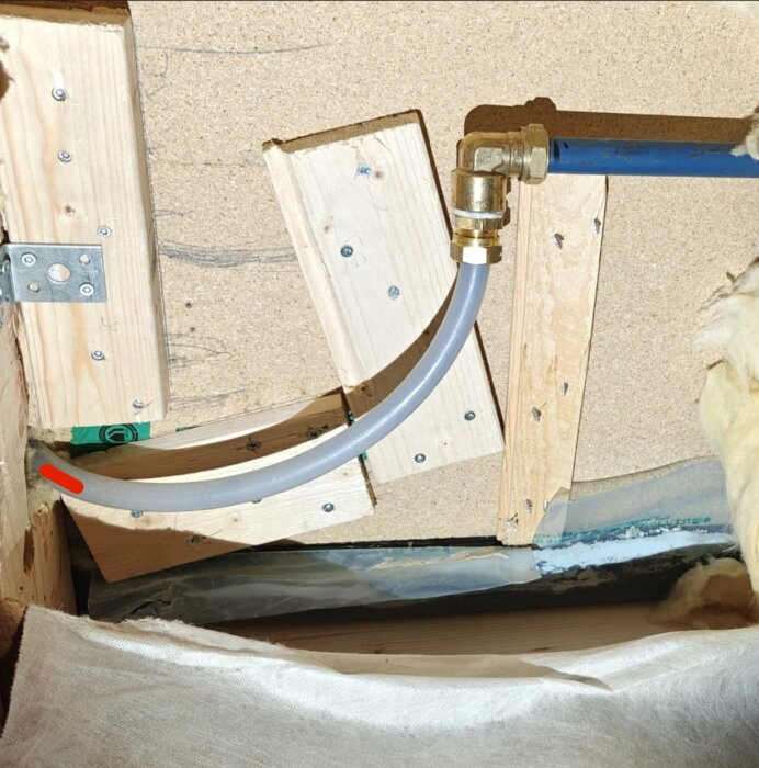 Röranslutning med böjt rör monterat på trästöd i ett utbrutet golv, med synlig isolering och träskiva.