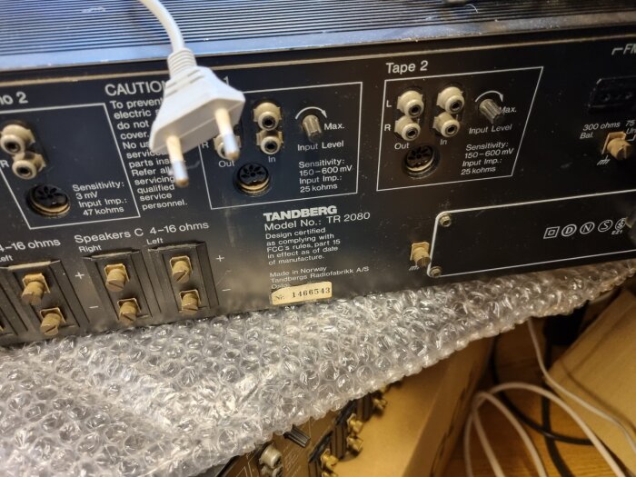 Baksidan av en Tandberg TR-2080 med olika anslutningar och en europakontakt ovanpå skyddsplast.
