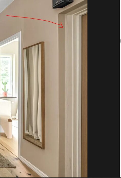 Spegel på vägg bredvid dörrkarm i hall med pil som pekar mot karmens ovansida.