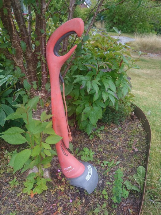 Röd trimmer av märket Flymo med gröna växter i bakgrunden.