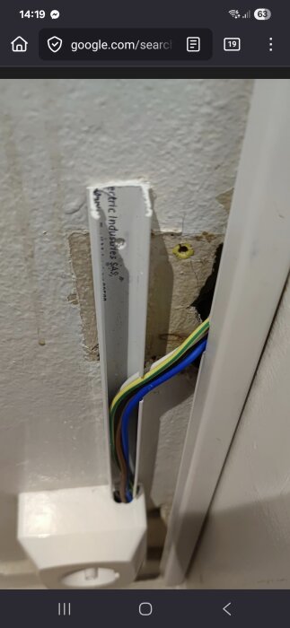 Öppen kabelkanal på vägg med synliga elledningar i olika färger, ovanpå en bit sliten vägg, nära ett eluttag.
