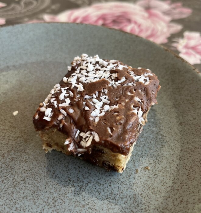 Brownie med chokladglasyr och kokosflingor på toppen, serverad på ett grått fat.