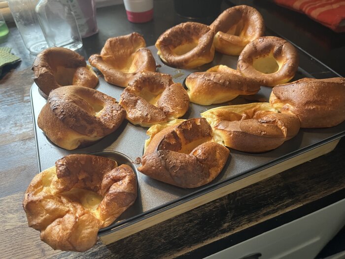 Pannkaksmuffins i muffinsform, gyllene och uppblåsta, nyligen uttagna ur ugnen på mörkt köksbord.