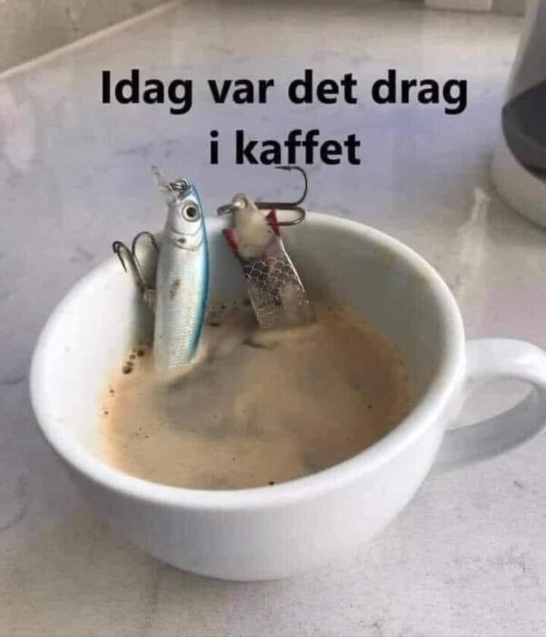 Kaffekopp med två fiskedrag nedsänkta i kaffet, bildtexten lyder "Idag var det drag i kaffet".