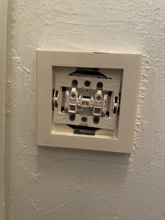 Väggbrytare utan täckplatta på en ljus vägg med exponerade skruvar och elektriska komponenter.
