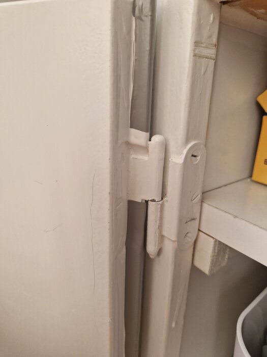 Gammalt gångjärn på kökslucka från 60-talet, inplastad och med färgslitage.