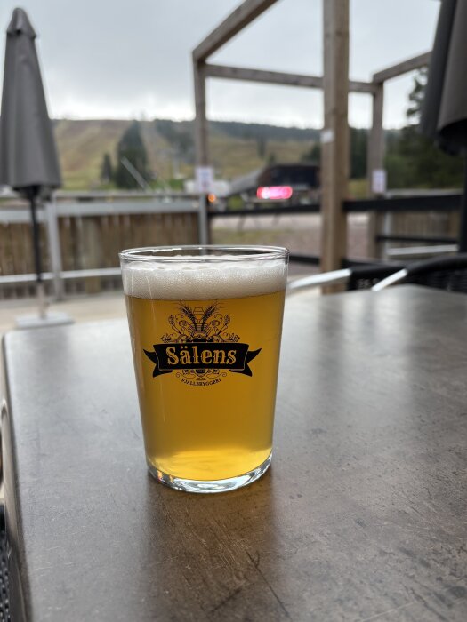 Ett glas med Lindvallen Pale Ale från Sälenfjällbryggeri står på ett utomhusbord, med bergsmiljö i bakgrunden.