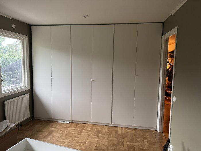 Garderober med vita dörrar uppställda i ett rum med parkettgolv, justerade efter montering.