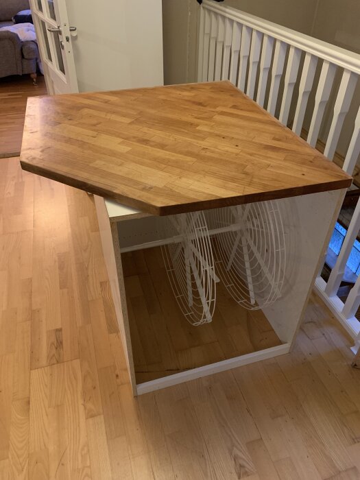 Träbordsskiva placerad över vit, öppen stomme med trähylla och synliga golvskydd i vardagsrum.