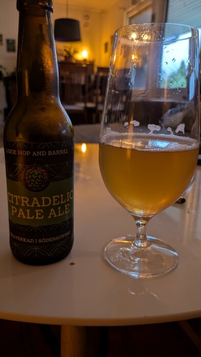 Flaska och glas med citradelic pale ale på bord i hemtrevlig miljö.