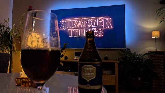 En TV visar "Stranger Things" med en flaska Chimay-öl och ett glas i förgrunden på ett bord.