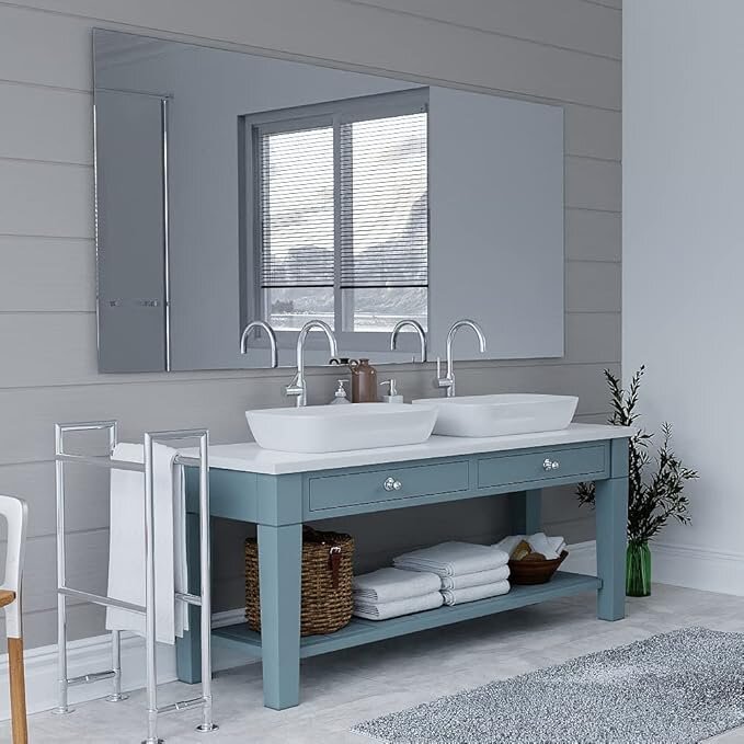 Badrum med två vita handfat på ett blått skåp, stor ramfri spegel utan beslag ovanför på väggen.