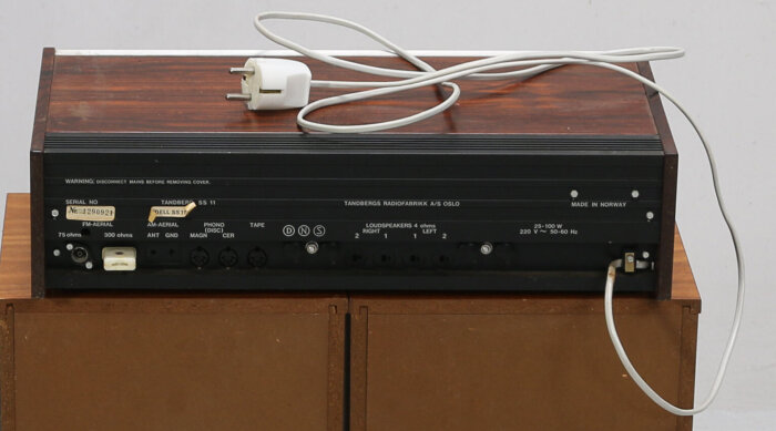 Baksida av en Tandberg förstärkare med olika ljud- och högtalaranslutningar, samt en strömkabel ovanpå.