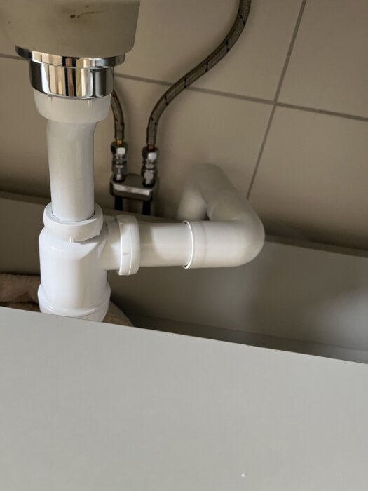 Plaströr och vattenlås under ett handfat i badrum, med synliga röranslutningar i väggen.