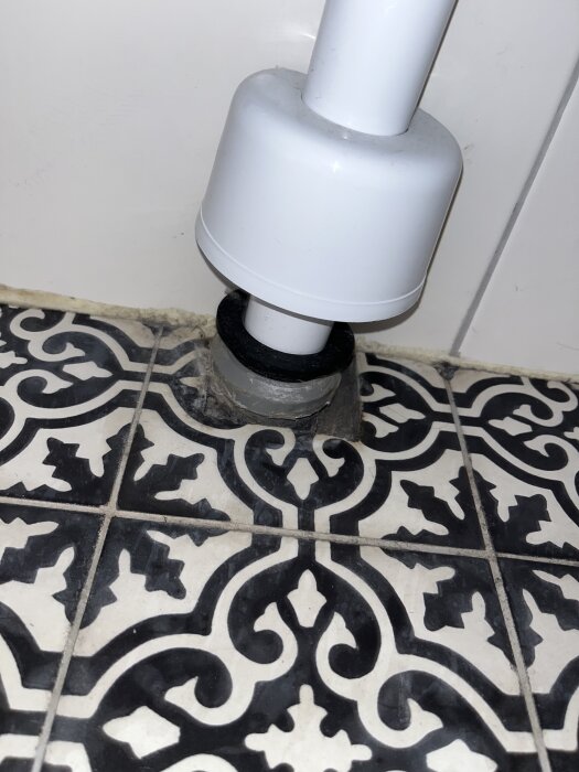 Avloppsrör från tvättställ i badrum med dekorativt kakelgolv, fokus på röranslutning vid golvnivå.