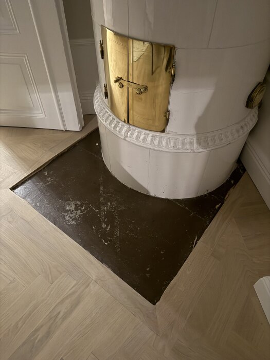 Kakelugn med guldluckor på trägolv, oskuret gnistskydd i behov av formning för halvcirkeln vid kakelugnen.