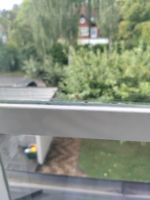 Närbild på ett fönster med synliga slipmärken i glaset. Utanför ses träd och ett rött hus i bakgrunden.