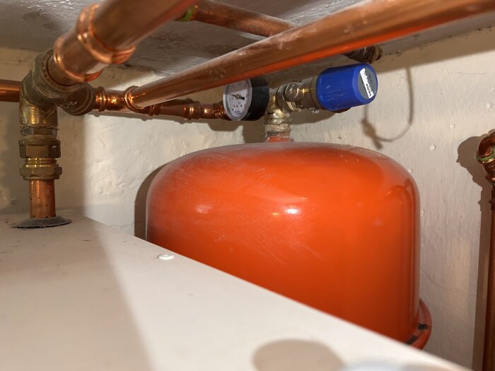 Varmvattenberedare med kopparrör och blått reglage vid en NIBE värmepanna i källare.