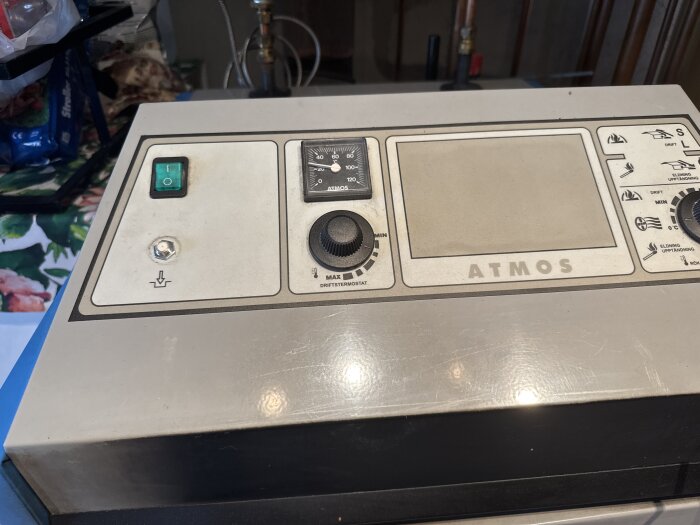 Kontrollpanel för vedpanna med Atmos-logotyp, strömbrytare och vred för inställningar.