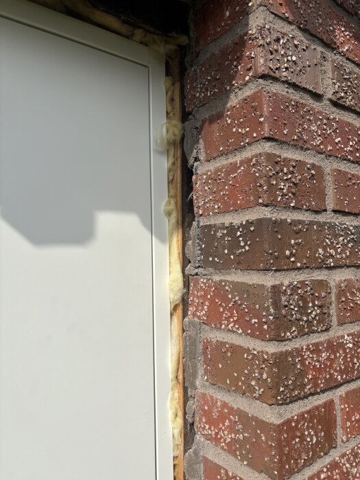 Nyinstallerad dörr till garage med synlig isolering mellan dörrkarm och tegelvägg.