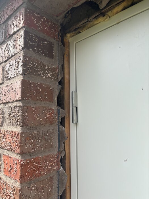 Nyinstallerad vit ytterdörr i isolerat garage, med synliga träreglar och murvägg. Fråga om bästa sätt att fuktskydda med list och eventuellt vindpapp.