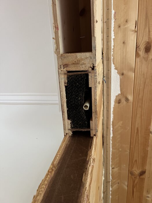 Detaljbild av byggelement i en vägg från 1969, visar ett dörrhål flyttat med en tigersåg; plankor fästa vid golvregel.