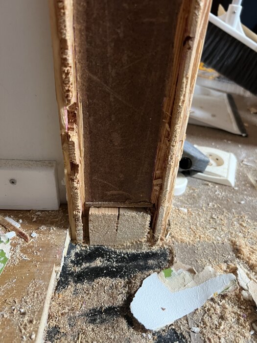 Detalj av byggelement i ett hus från 1969, visar träkonstruktion i dörrhål med synliga spånskivor och sågspån på golvet.