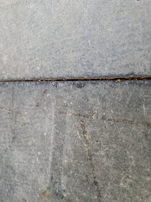 Närbild av två gråa, texturerade plattor på altanen, med en smal spricka emellan som antyder eventuell asbestinnehåll.