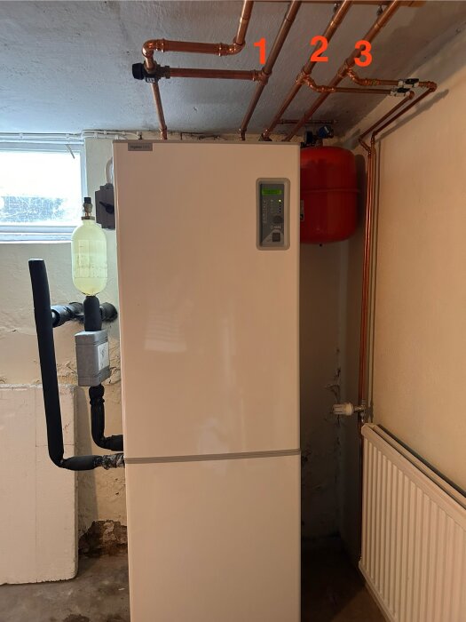 Värmepump i ett rum med kopparrör märkta 1, 2 och 3, samt en röd expansionstank och en ventil nära rör 1.