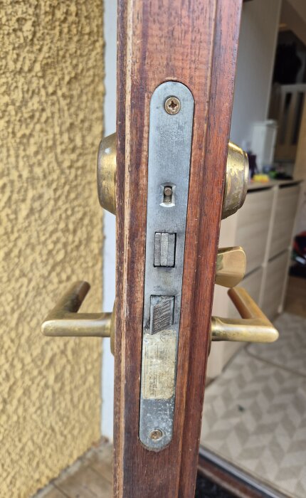 Närbild av en äldre dörrs lås och handtag i ett radhus, med fokus på metallbeslaget och träet runt låset.