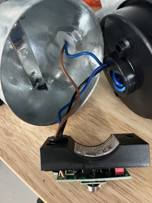 Två kablar, brun och blå, är dragna mellan lampans komponenter och en separat svart sensorhölje.