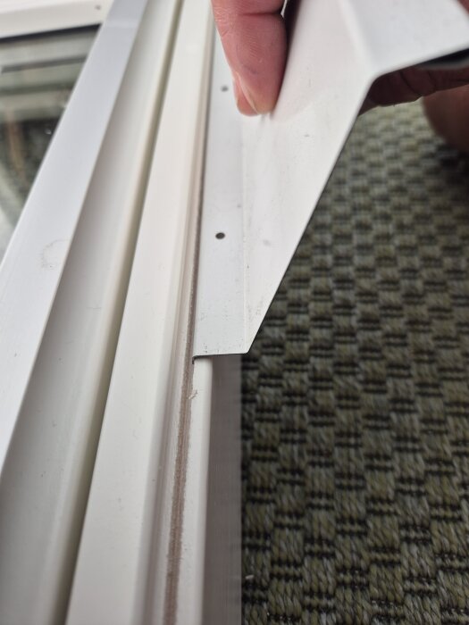 Närbild på hand som håller ett vitt underbleck bredvid en Solid Elements-fönsterkarm. Bleckets hål syns utanför fönsterkarmens skåra.